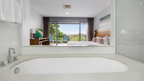 Ein modernes Hotelzimmer mit einer großzügigen Badewanne, einem Balkon mit Aussicht und einem Fernseher.