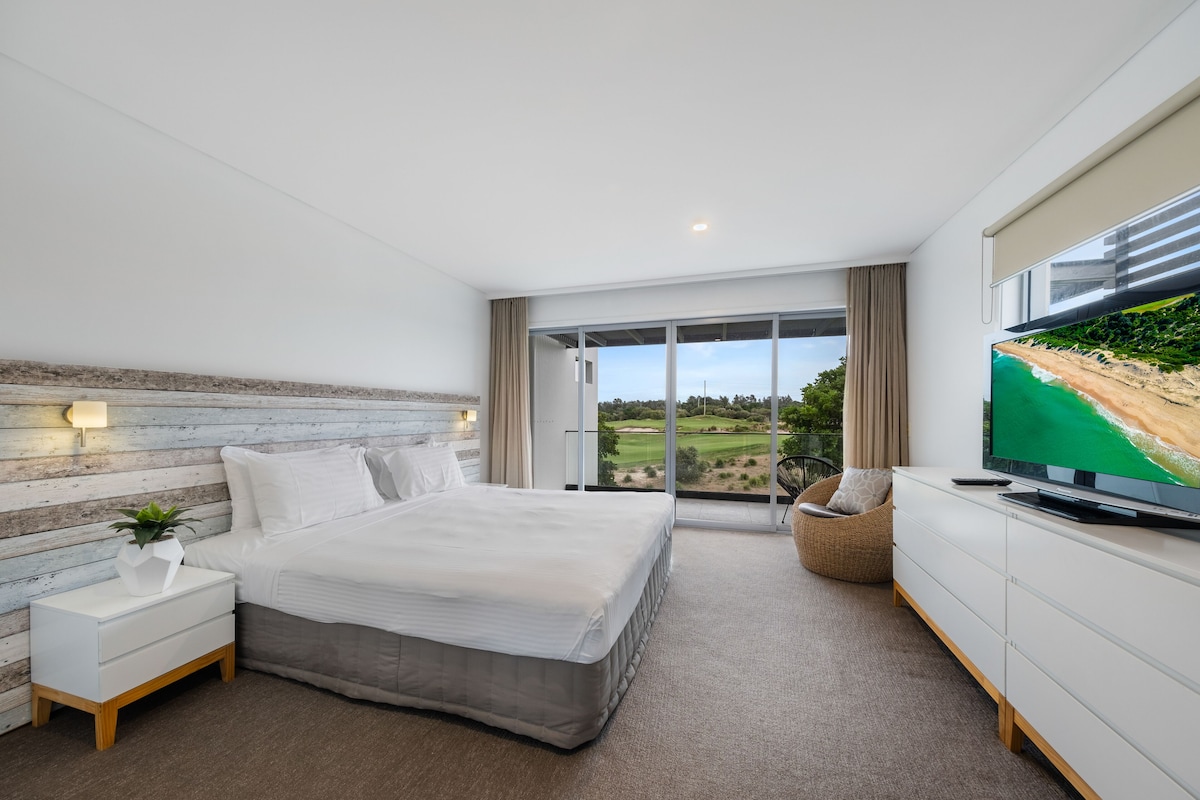 A modern bedroom with a large bed, a TV, and a view of a golf course.