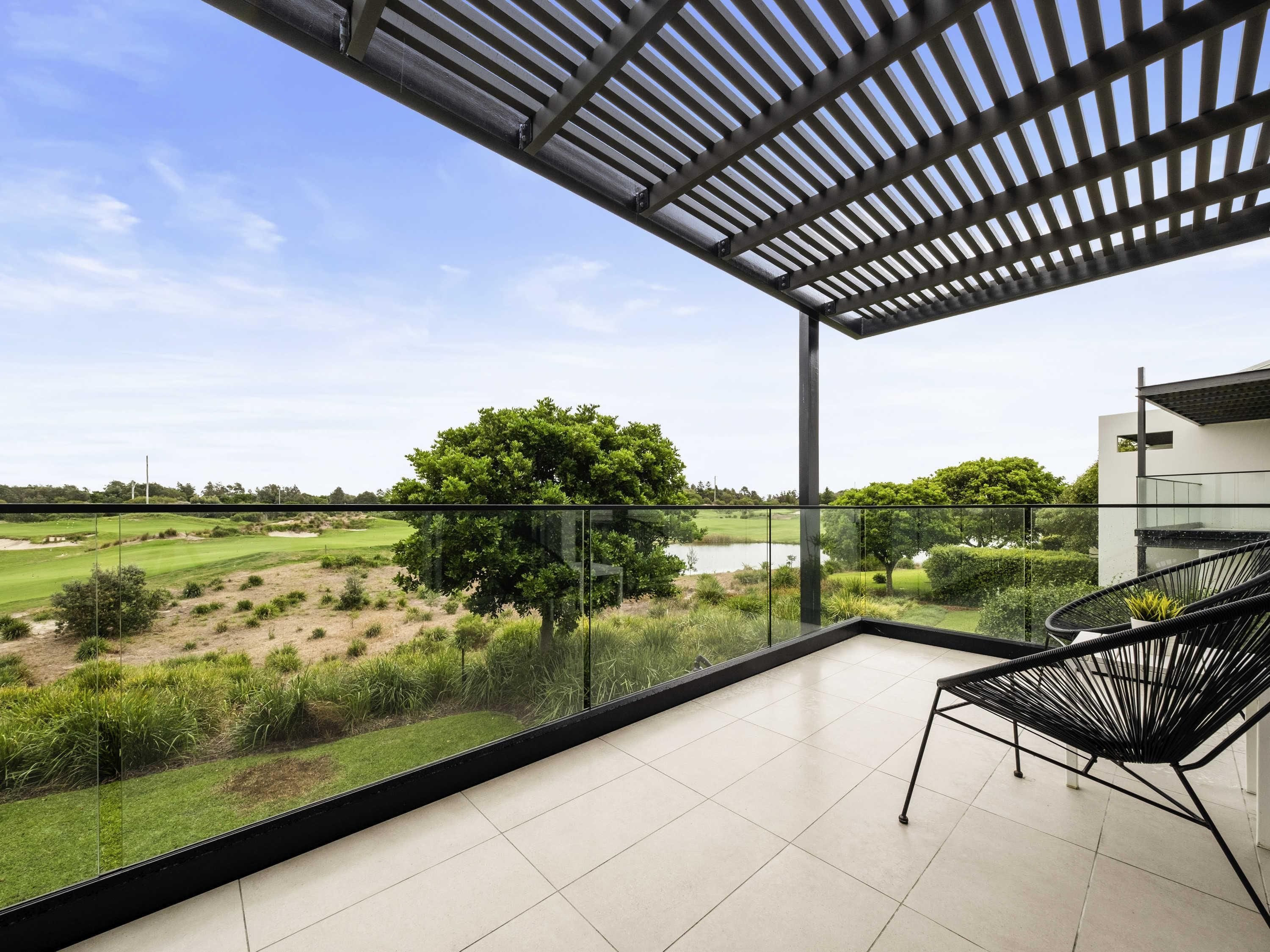 Un balcón con vista a un campo de golf, un árbol y un edificio moderno.