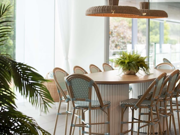 A round dining table with wicker chairs, a hanging light fixture, and a potted plant on the table.