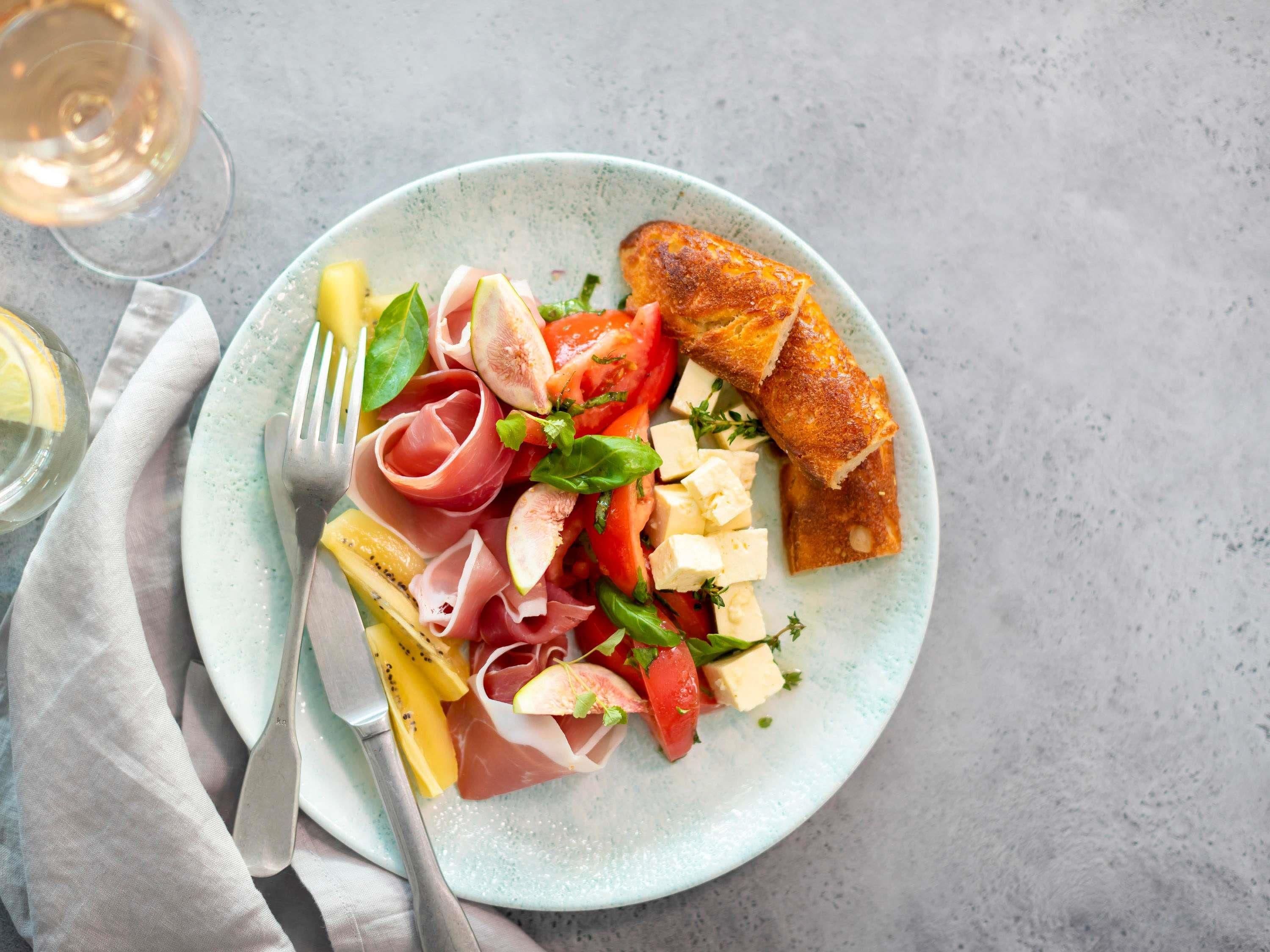 A plate with various foods and a glass of white wine.