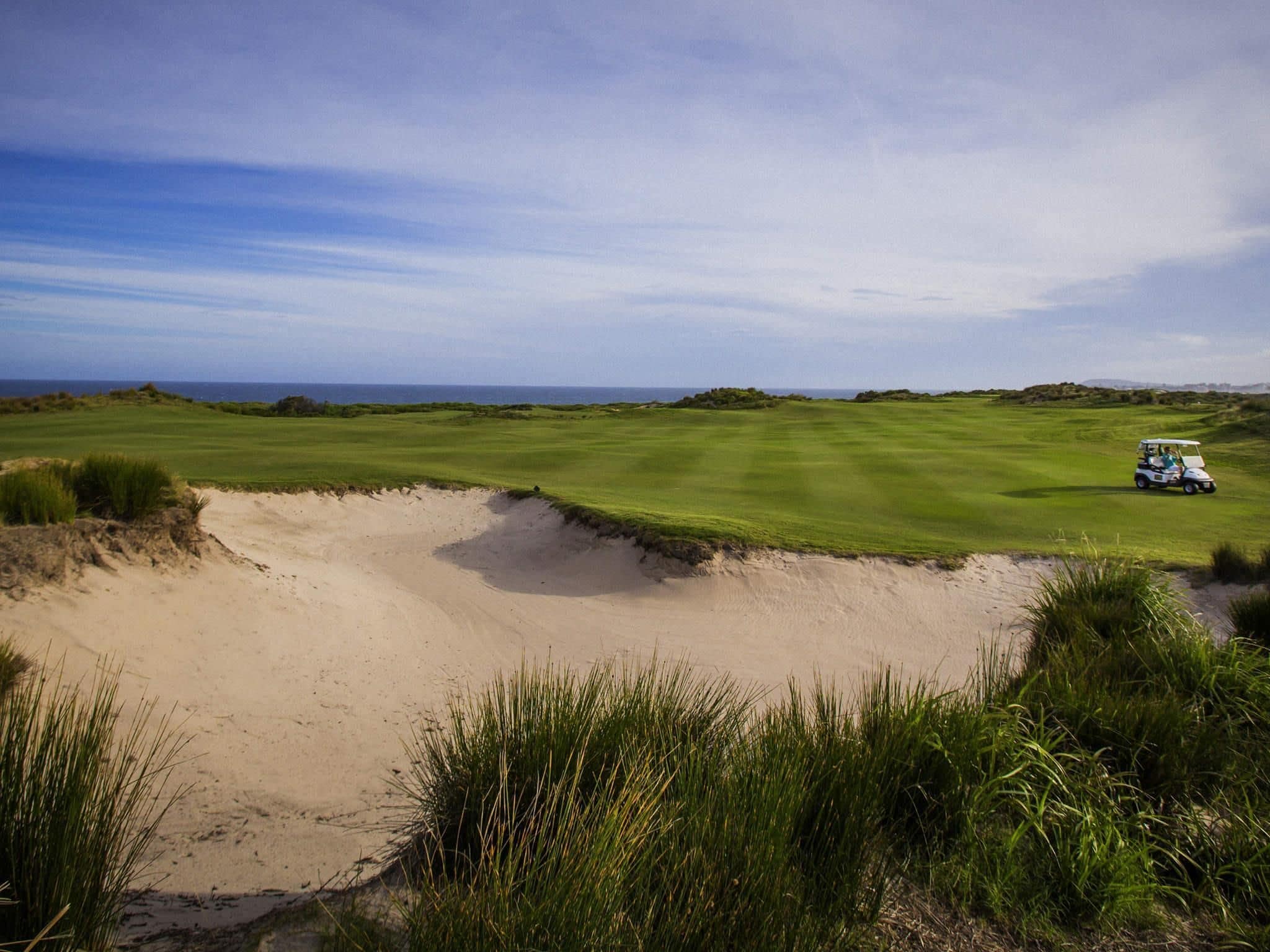 A golf course with a sand bunker and a golf cart.
