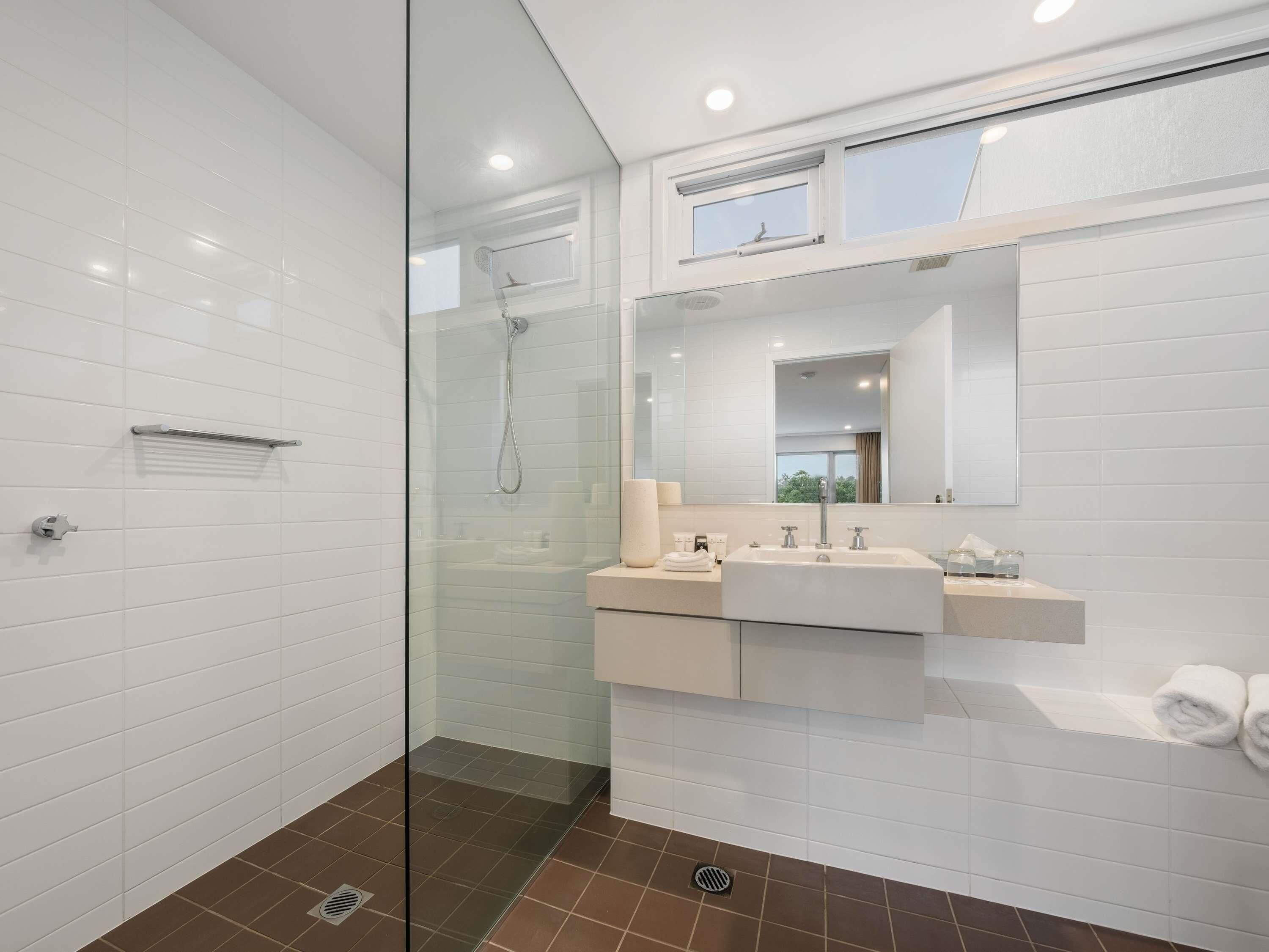 A modern bathroom with a glass shower enclosure, a vanity with a sink and mirror, and a window above the mirror.