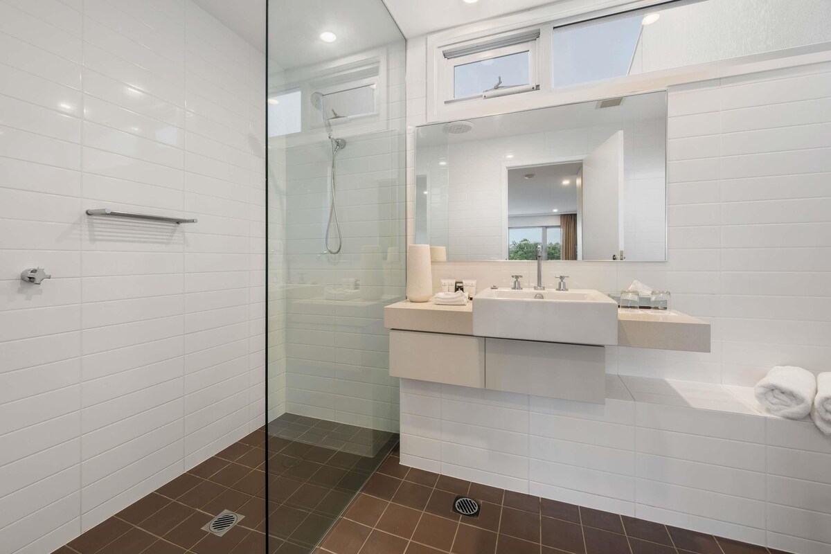 A modern bathroom with a glass shower enclosure, a vanity with a sink and mirror, and a window above the mirror.