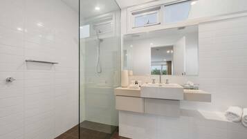 A modern bathroom with a glass shower enclosure, a vanity with a sink and mirror, and a window above the mirror.