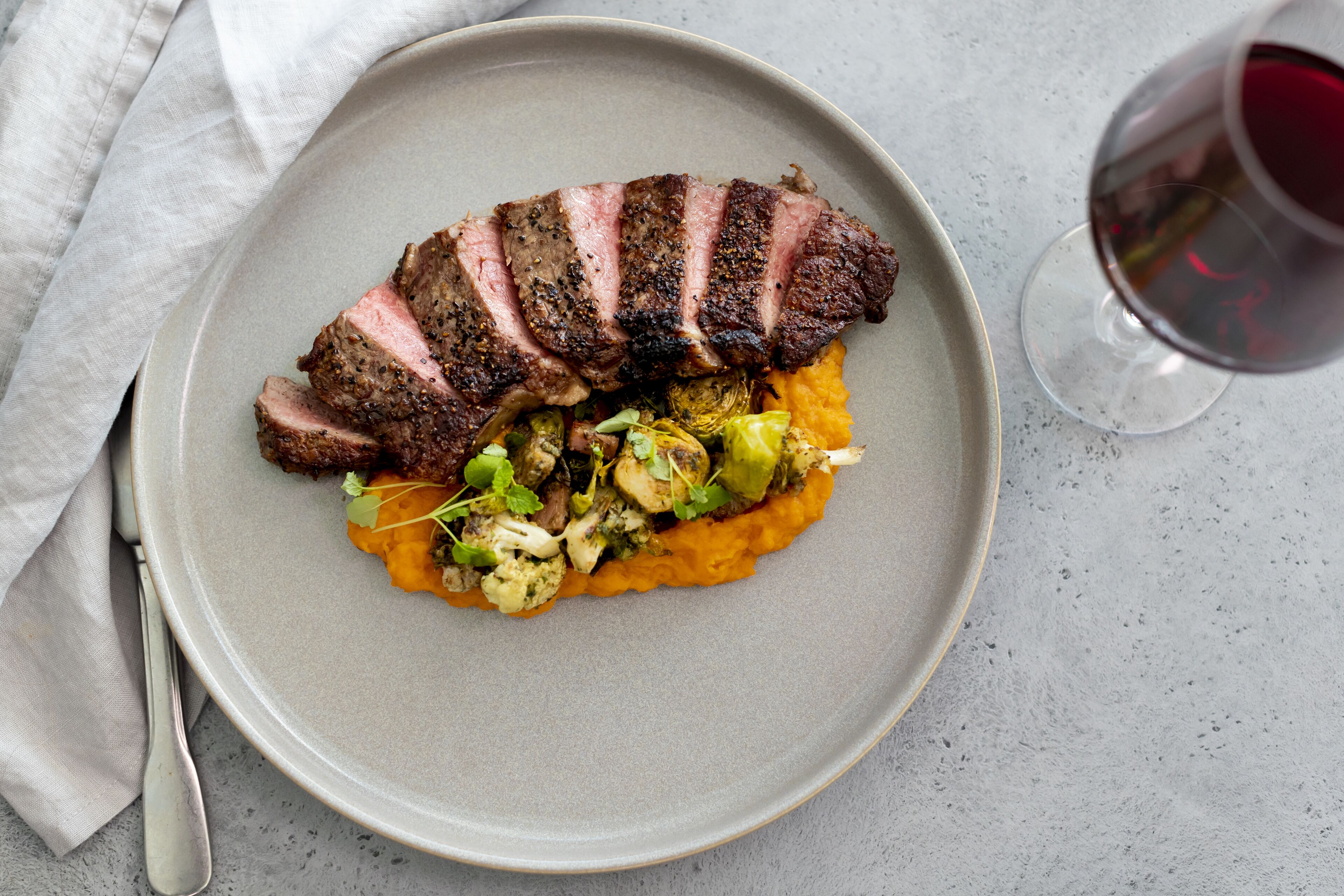 A plate with sliced meat, vegetables, and a glass of red wine.