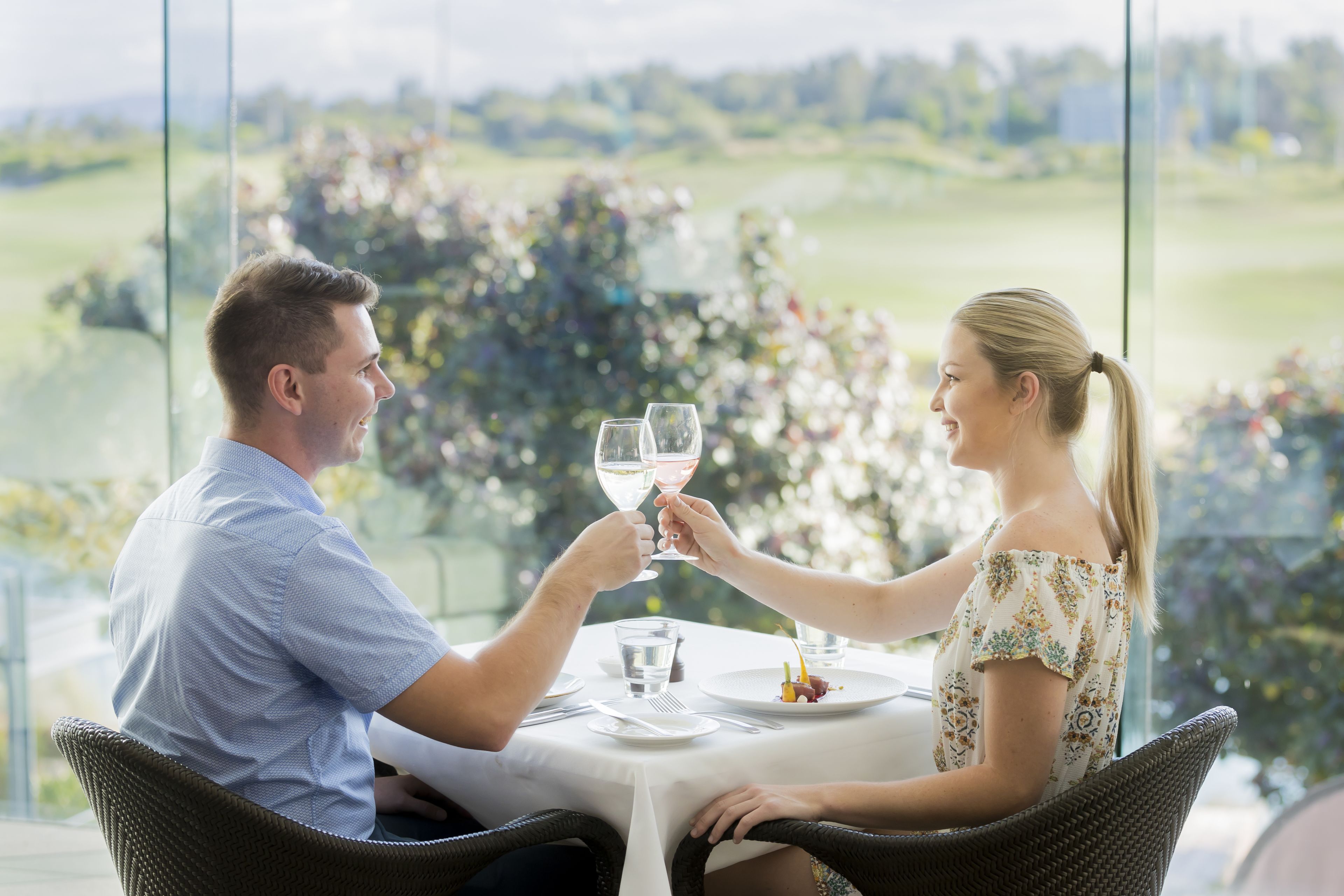 Een koppel proost met wijnglazen aan een tafel met uitzicht op een golfbaan.