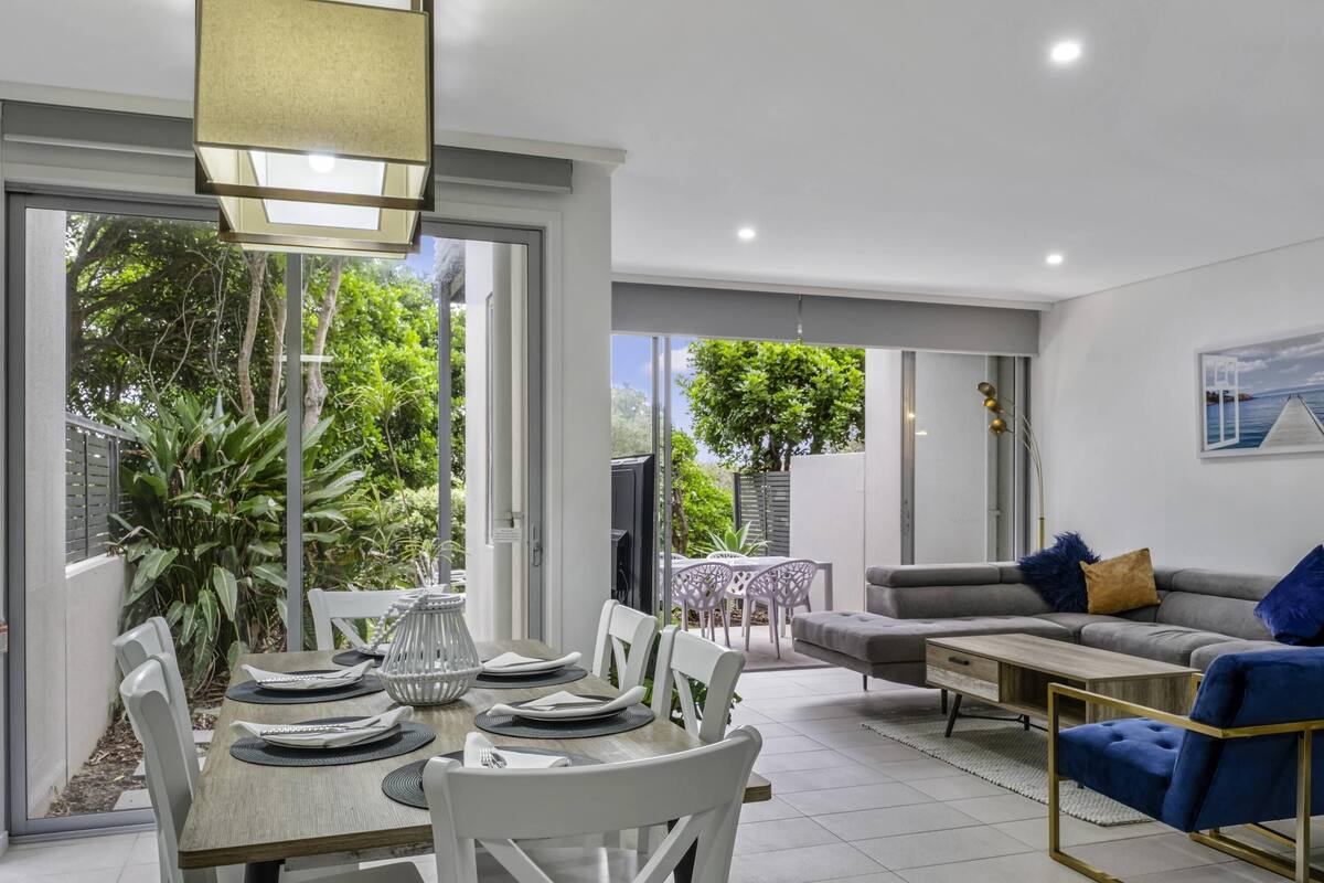 Un salon moderne comprenant un coin repas, un canapé et une vue sur la verdure environnante.