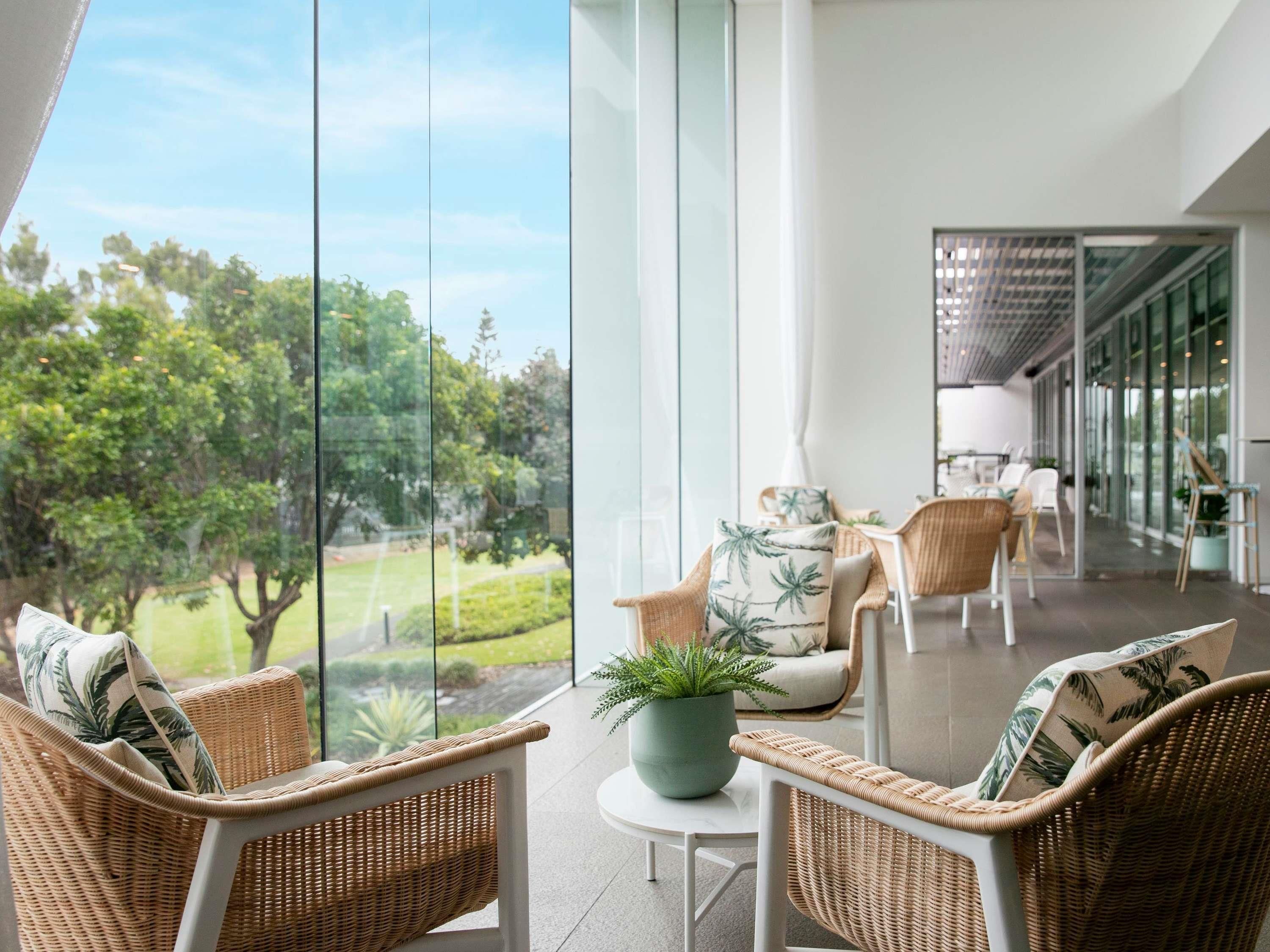 A modern indoor space with wicker furniture, a potted plant, and a view of greenery outside.