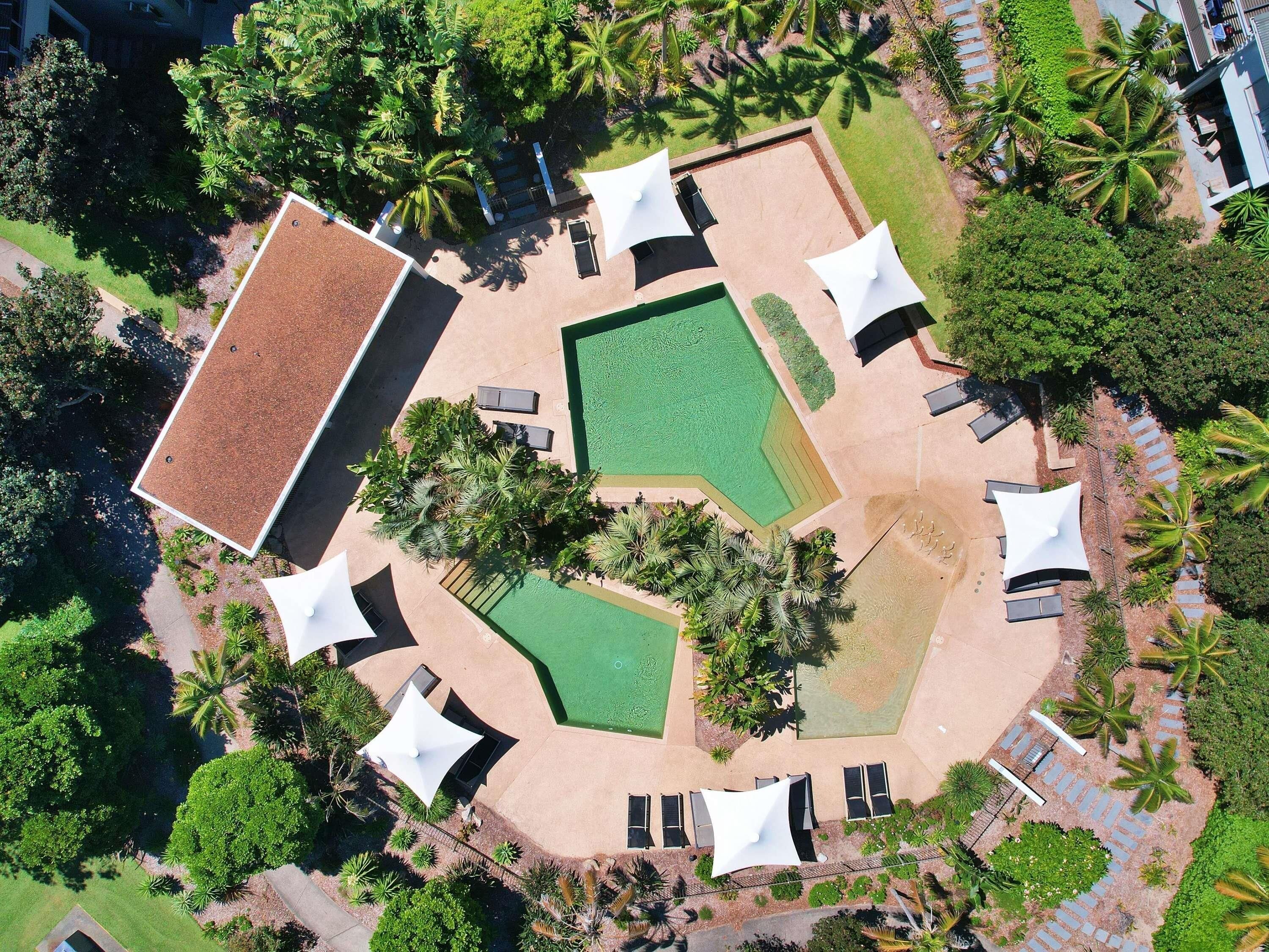 An aerial view of a resort with multiple pools, sun loungers, and palm trees.