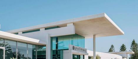 Un edificio moderno con fachada de vidrio, un letrero que dice 'Pullman' y una zona cubierta con vehículos estacionados afuera.
