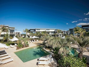 A resort with multiple modern buildings, a central swimming pool, and lounge areas with umbrellas. - Pullman Magenta Shores Resort (Magenta Shores)