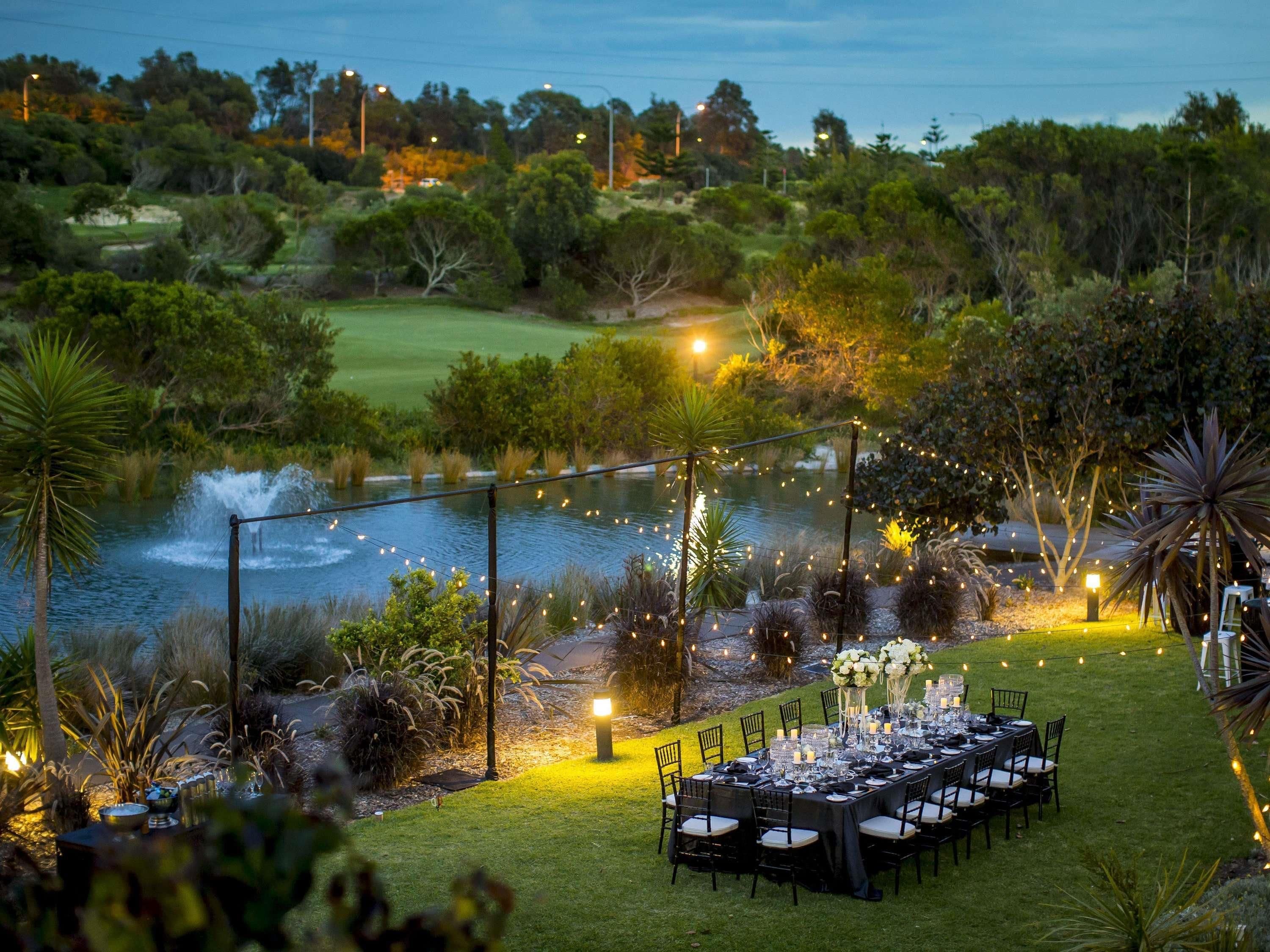 An outdoor dining area with a table set for a meal, surrounded by greenery and a body of water.