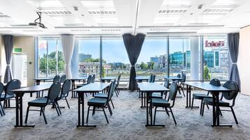 Un salón de conferencias con mesas y sillas, ventanas amplias con vista a la ciudad y un diseño moderno de techo.