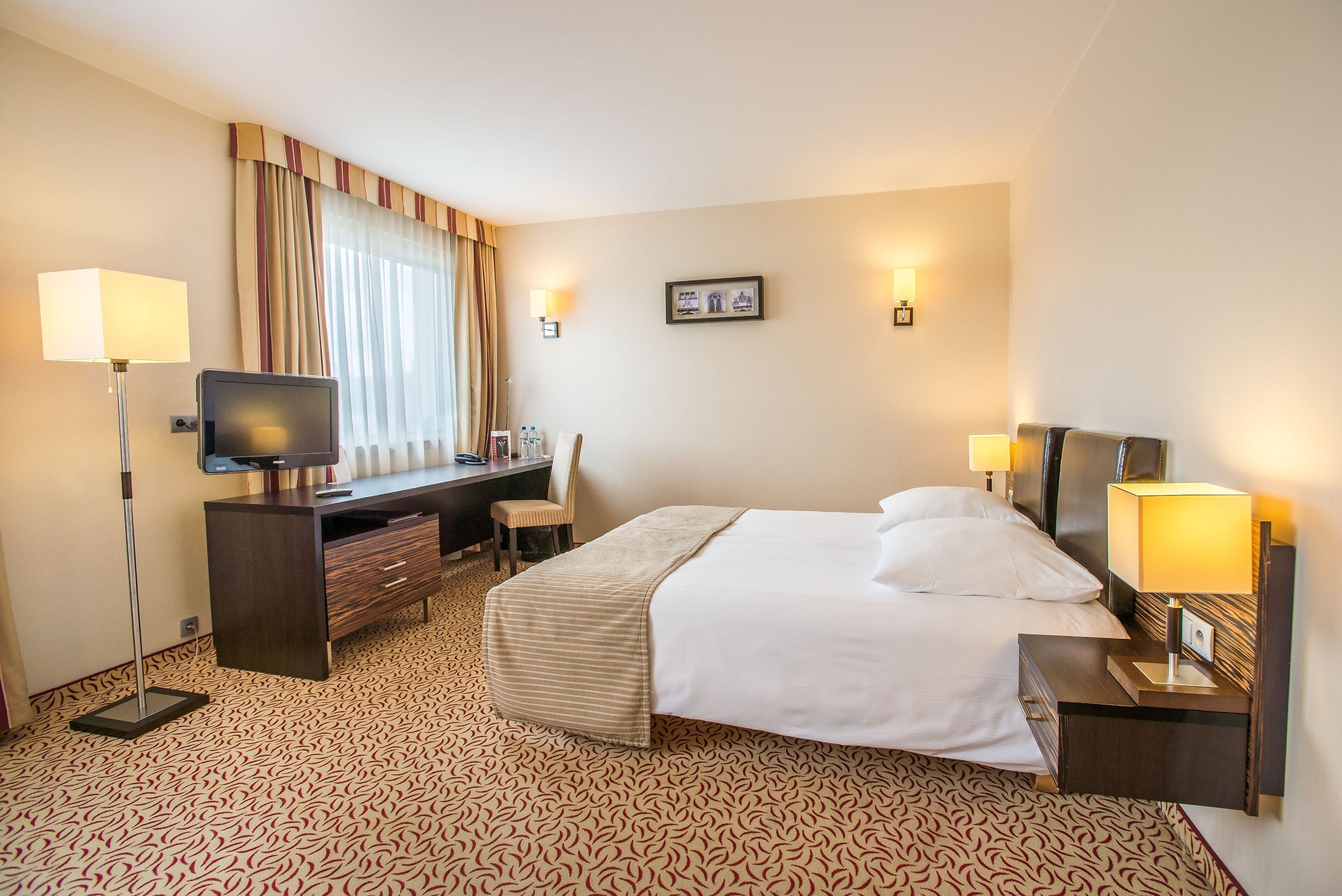 Een hotelkamer met een bed, bureau, stoel, televisie en lampen.