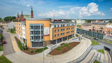 A modern hotel with a central courtyard, a prominent clock tower in the background, and a clear sky.