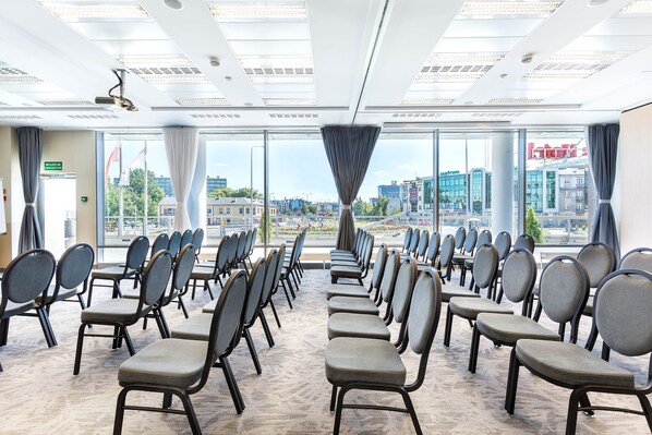 A conference room with rows of chairs facing a large window with a city view.