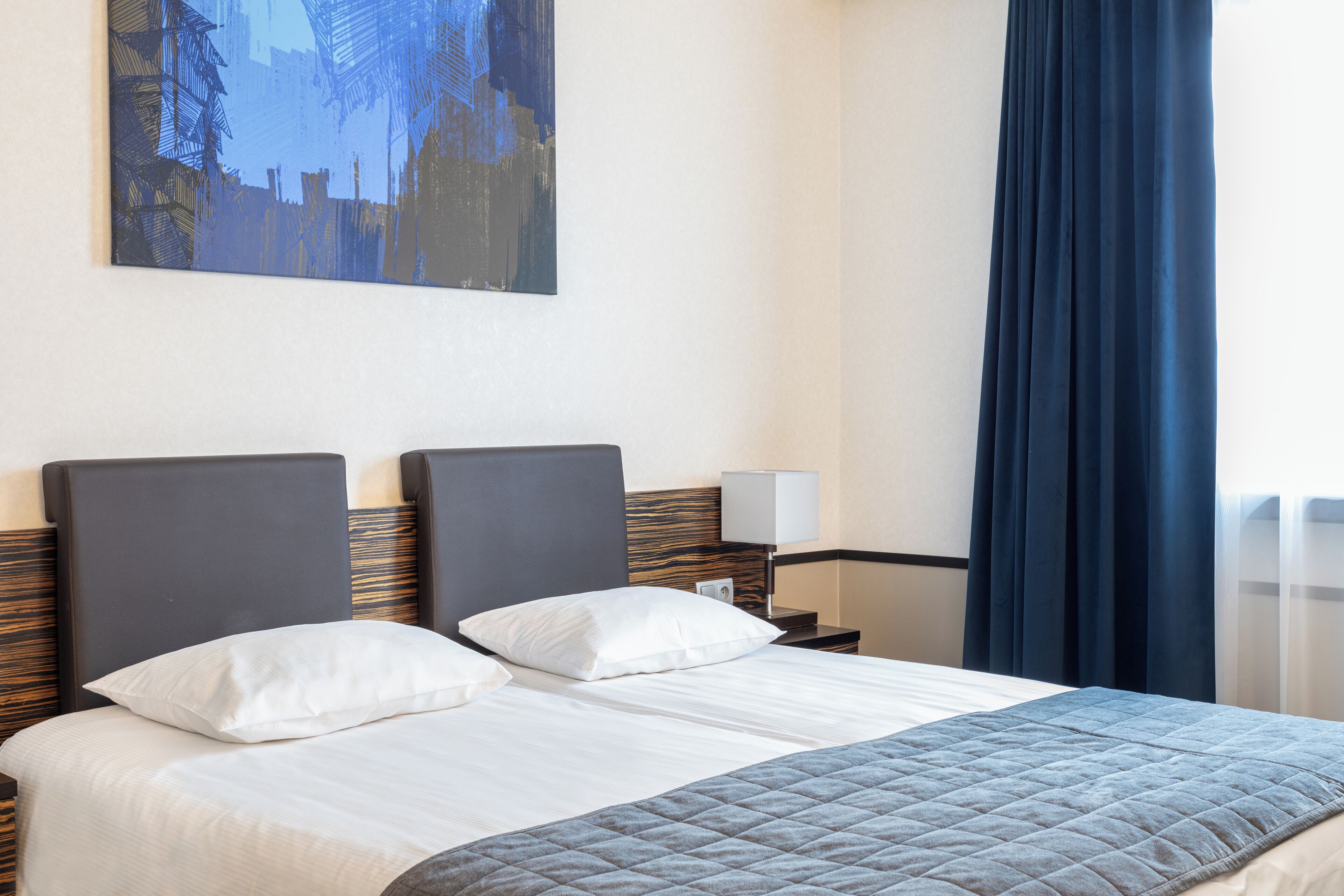 A hotel room with a large bed, two pillows, a bedside table with a lamp, and a painting on the wall.