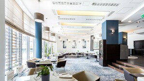 A modern hotel dining area with tables set for dining, large windows, and a view of the city. - Qubus Hotel Kielce (Kielce)