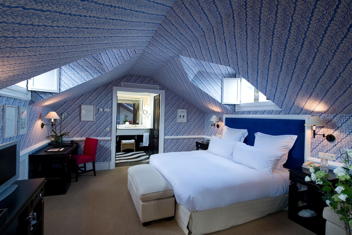 A bedroom with a sloped ceiling, a bed, a desk, a chair, and a mirror.