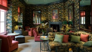 Un salon chaleureux avec un papier peint à motifs floraux, une cheminée et des fauteuils confortables.