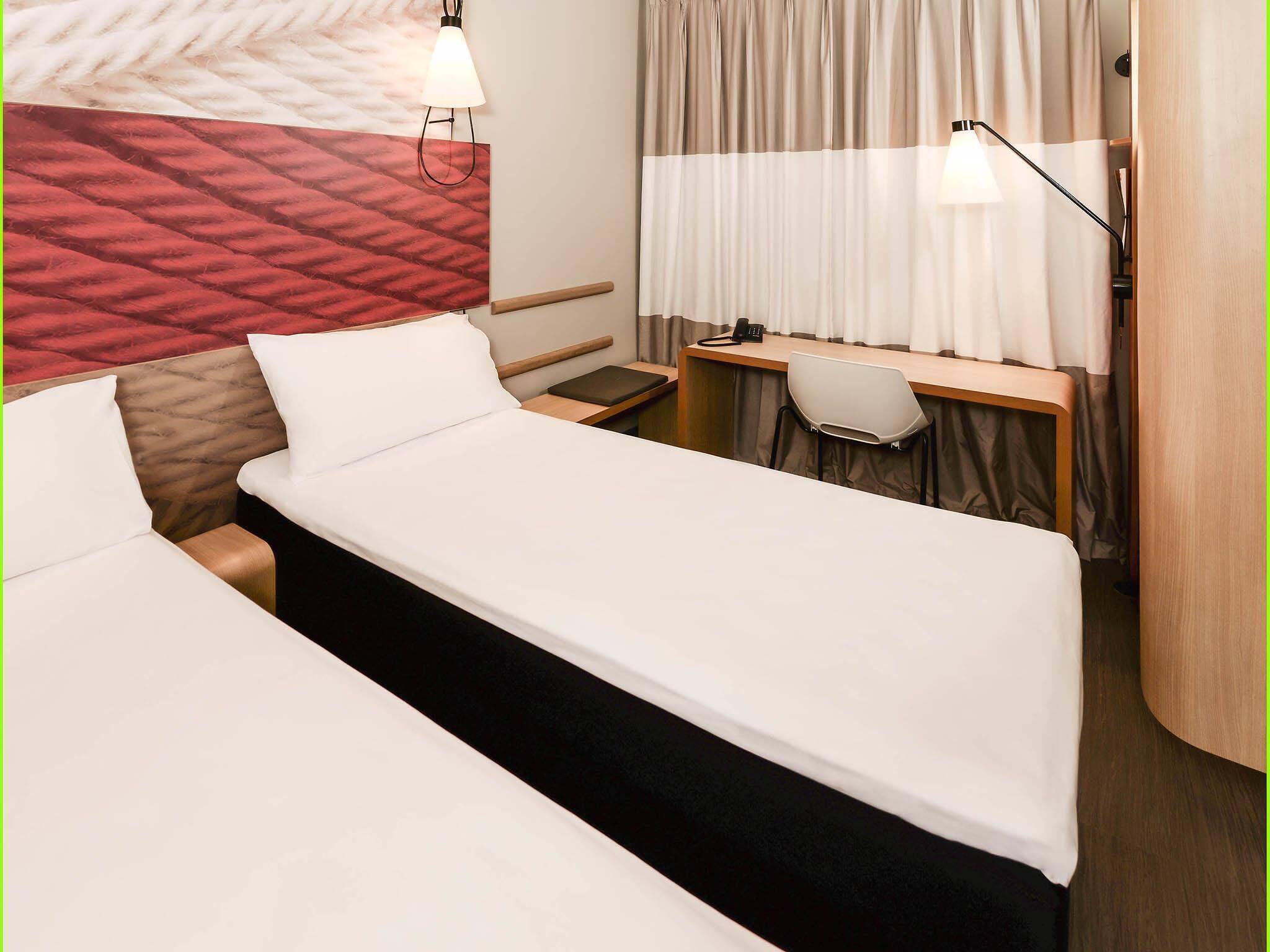 Ein Hotelzimmer mit zwei Betten, einem Schreibtisch mit Stuhl, einem Telefon und einer Lampe.