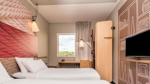 A hotel room with two beds, a desk, a TV, and a large window with a view of greenery. - ibis Campo Grande (Campo Grande)