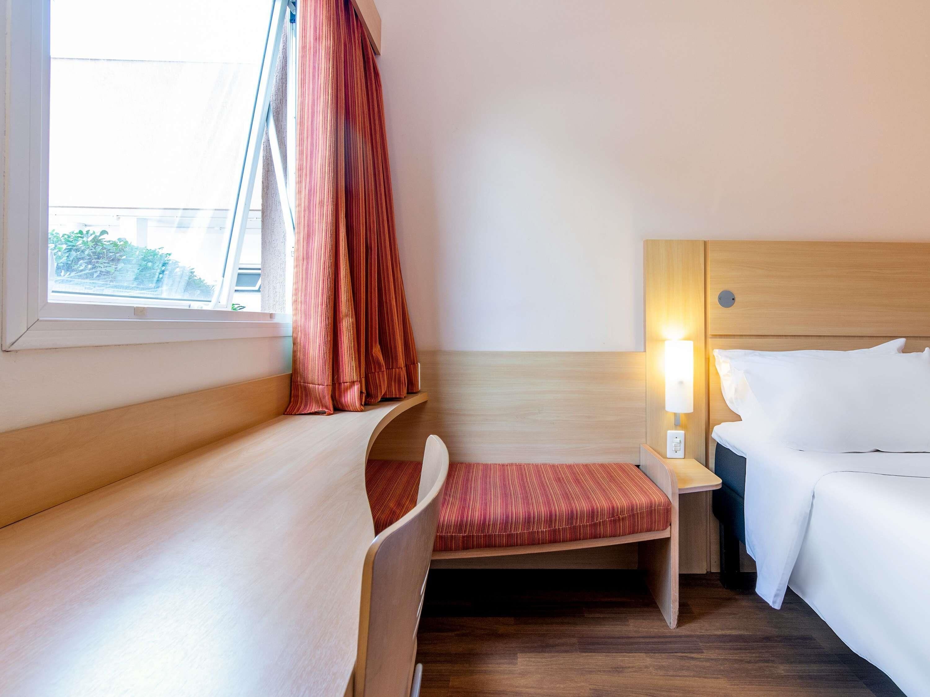 Una habitación de hotel con una cama, un escritorio, una silla, una mesita de noche y una lámpara.