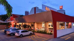 A modern hotel with a red and white facade, a parking area with white cars, and a visible restaurant or dining area with outdoor seating. - ibis Campo Grande (Campo Grande)