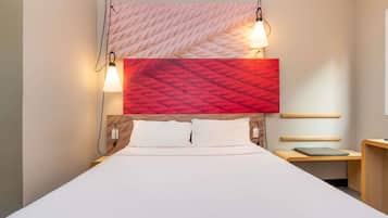 Une chambre d’hôtel avec un grand lit, deux lampes de chevet, une décoration murale rouge à motifs et une petite table de chevet avec une lampe.