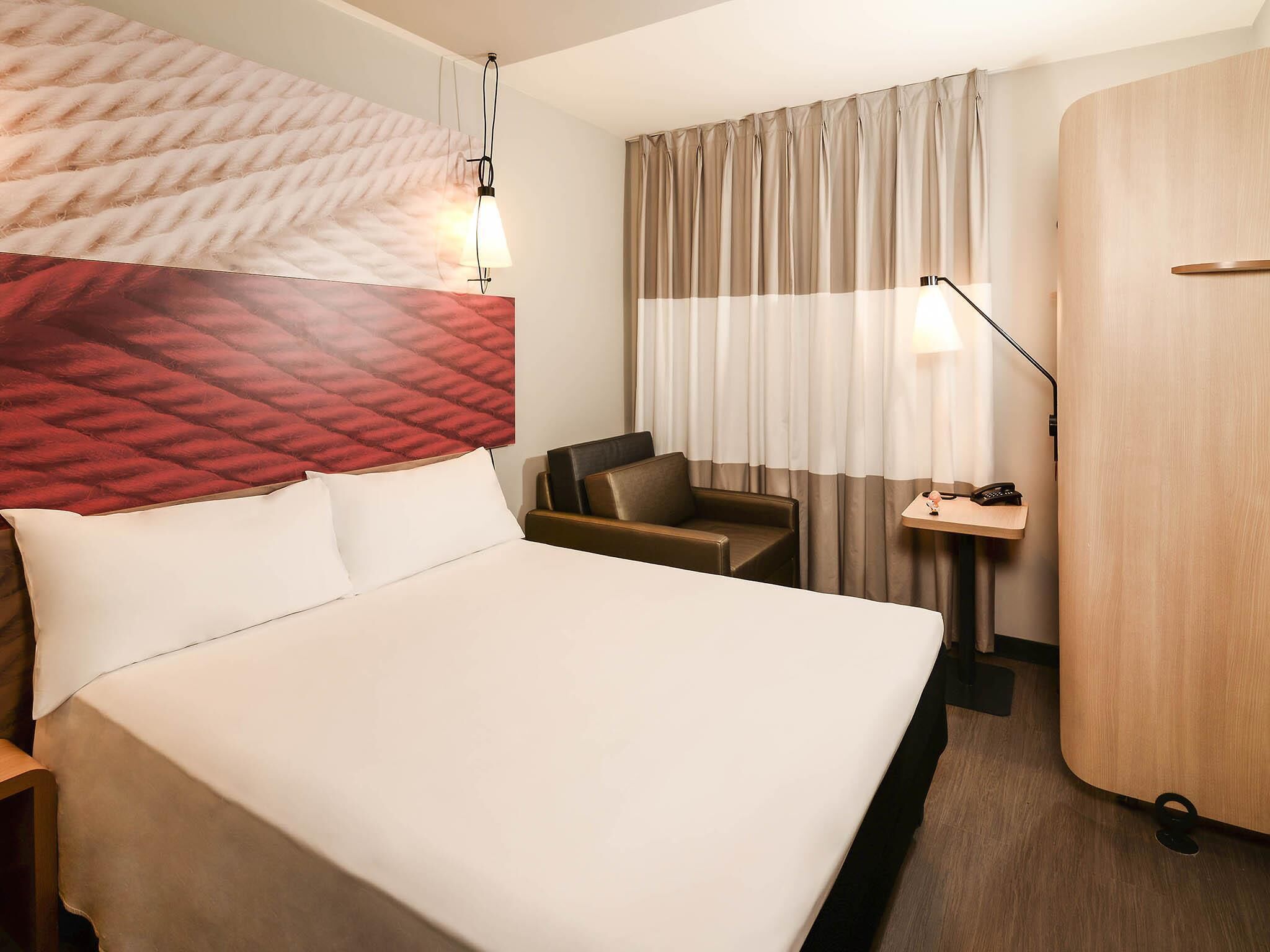 Una habitación de hotel con una cama grande, un escritorio con lámpara, una silla y un armario.