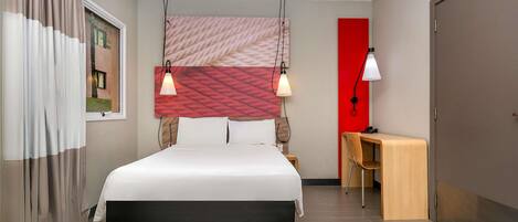 Una habitación de hotel moderna con una cama grande, un escritorio y una pared de acento roja.