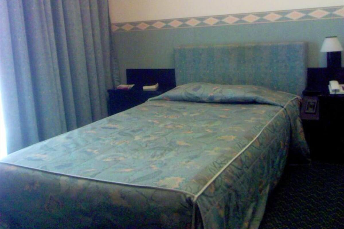 A hotel room with a bed, a nightstand, a lamp, and a window with curtains.