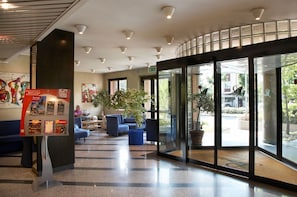 A modern lobby with a reception desk, seating area, and large glass doors leading outside. - Pacific Hotel Airport (Borgaro Torinese)