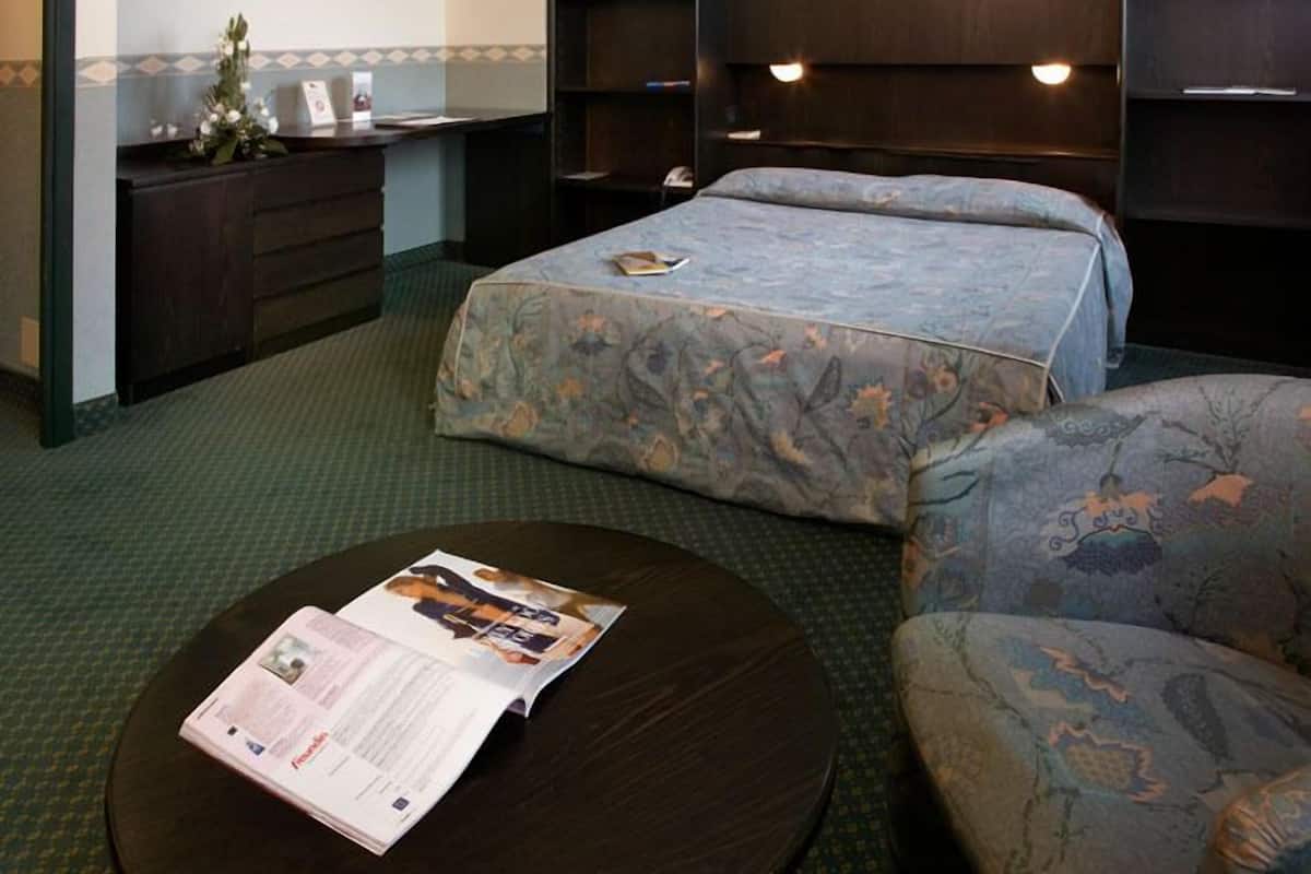 A hotel room with a bed, a desk, a chair, a round table, and a bookshelf.