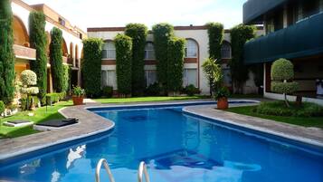 A swimming pool with a metal ladder, surrounded by well-maintained greenery and a building with multiple windows and balconies.