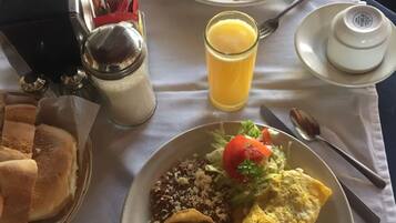 Uma mesa posta com dois pratos de comida, um copo de suco de laranja, saleiros e pimenteiros, uma cesta de pão e uma pequena tigela.
