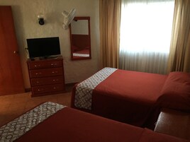 Habitación de hotel con dos camas, un televisor en una cómoda, un espejo y una ventana con cortinas.