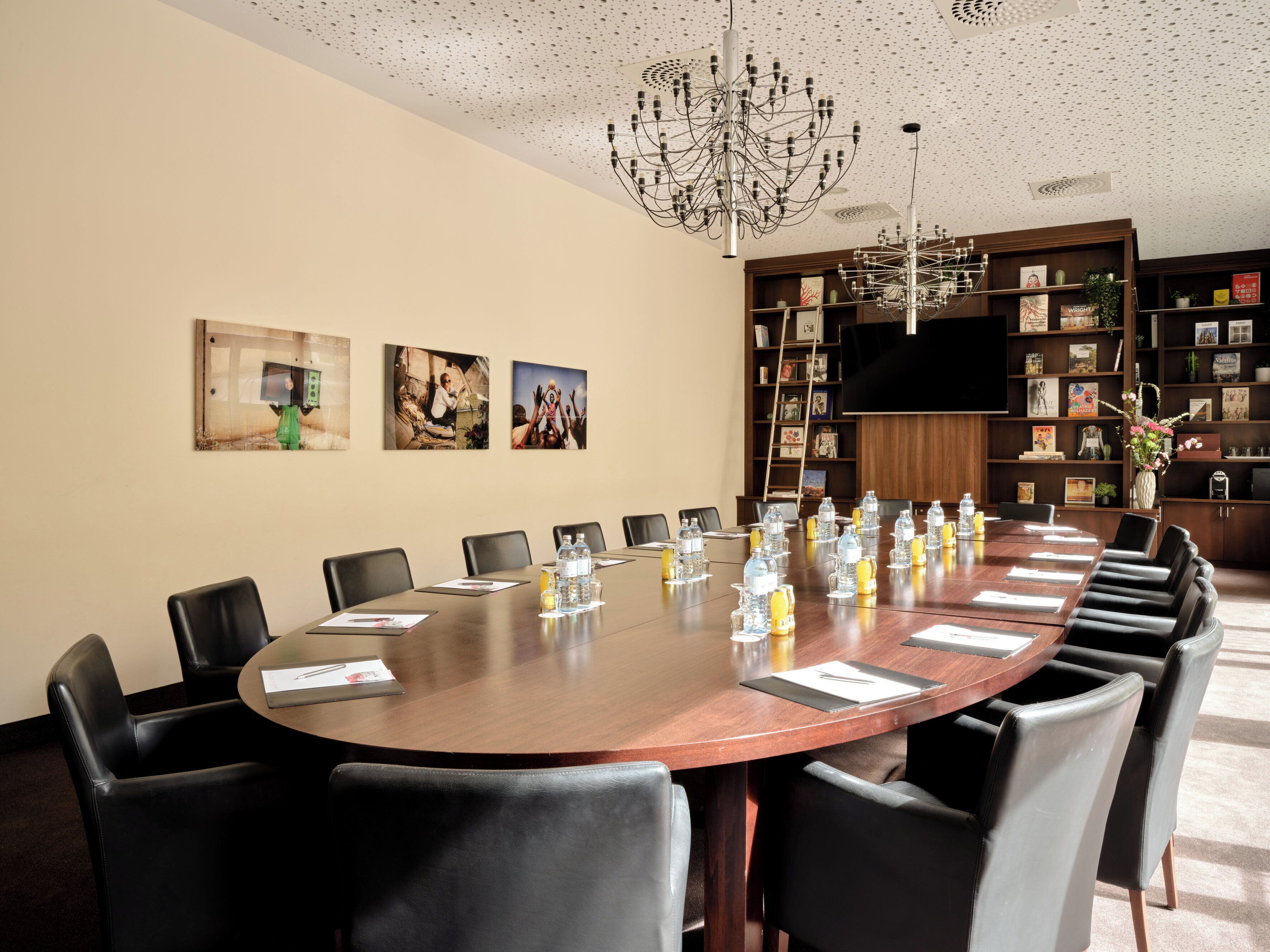 A conference room with a large wooden table, black leather chairs, and a chandelier.