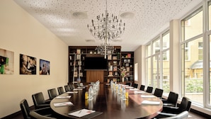 Een vergaderruimte met een ronde tafel, zwarte leren stoelen en een groot raam met uitzicht op het buiten.