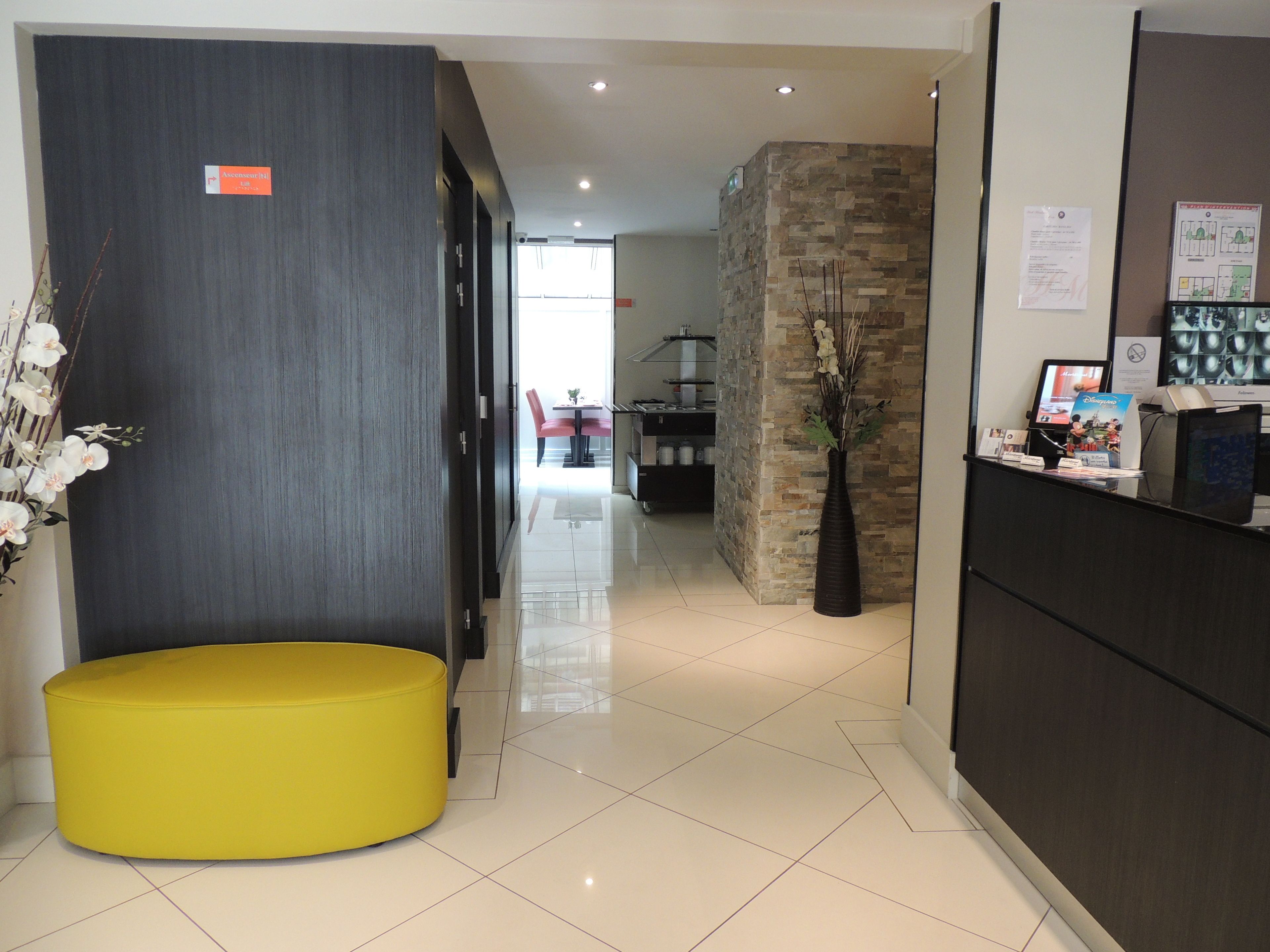 Un vestíbulo de hotel con una recepción, una zona de estar amarilla y una pared de acento de piedra.