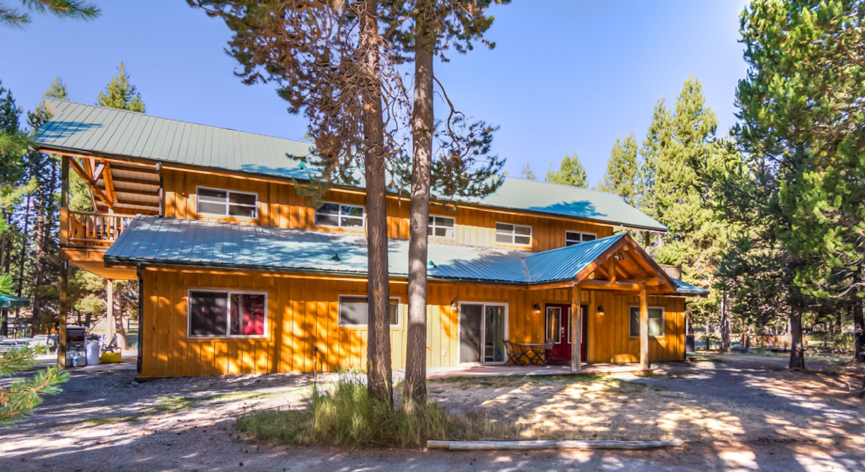 A two-story log cabin with a green roof, surrounded by trees.