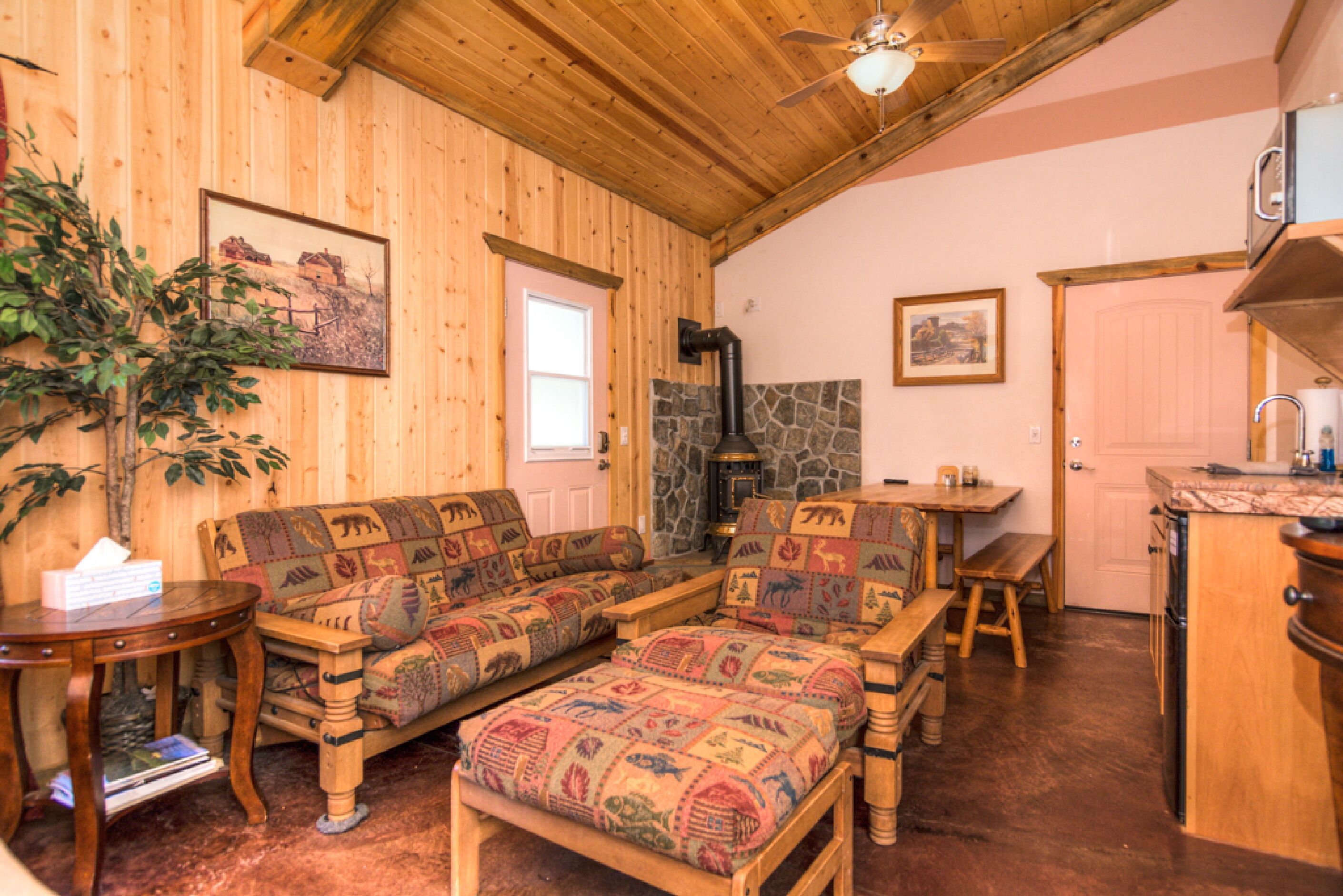 L’intérieur d’un chalet confortable, avec un plafond en bois, une cheminée en pierre, une table à manger en bois et un ensemble de canapés.