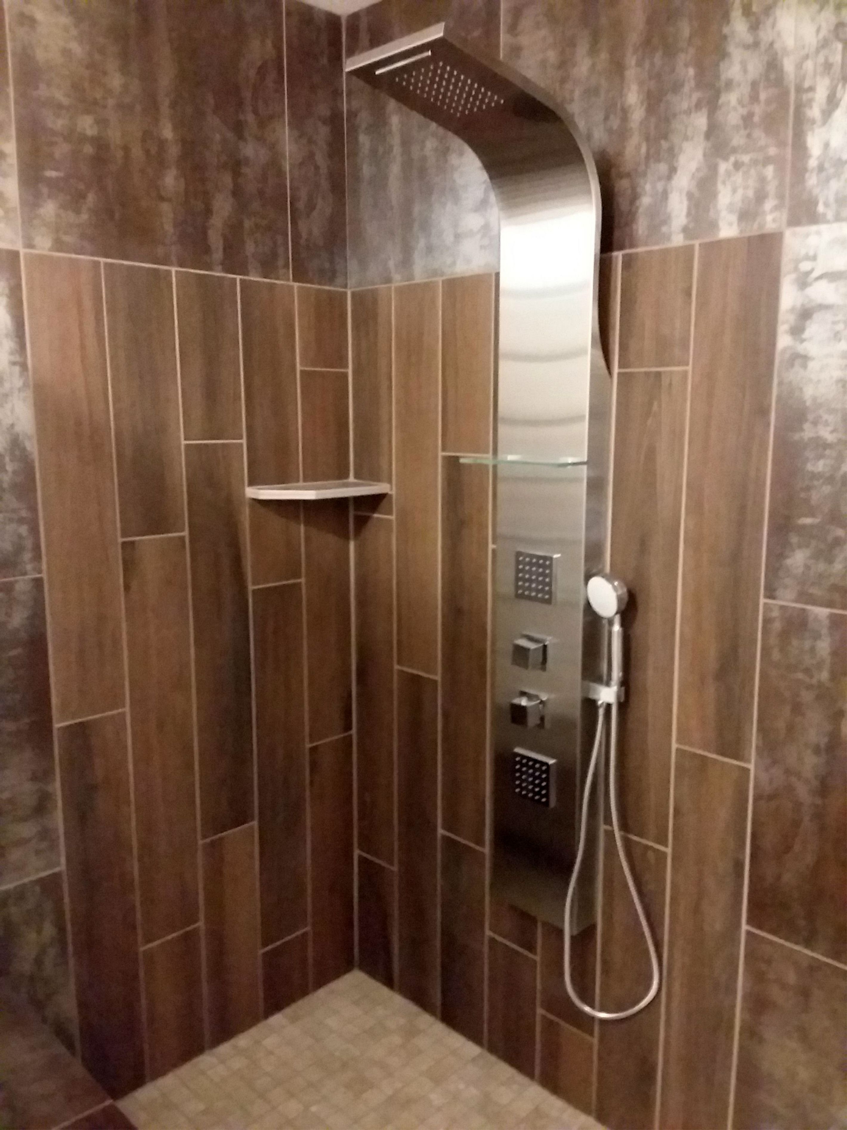 A shower with a curved overhead design, a control panel, and a handheld showerhead.