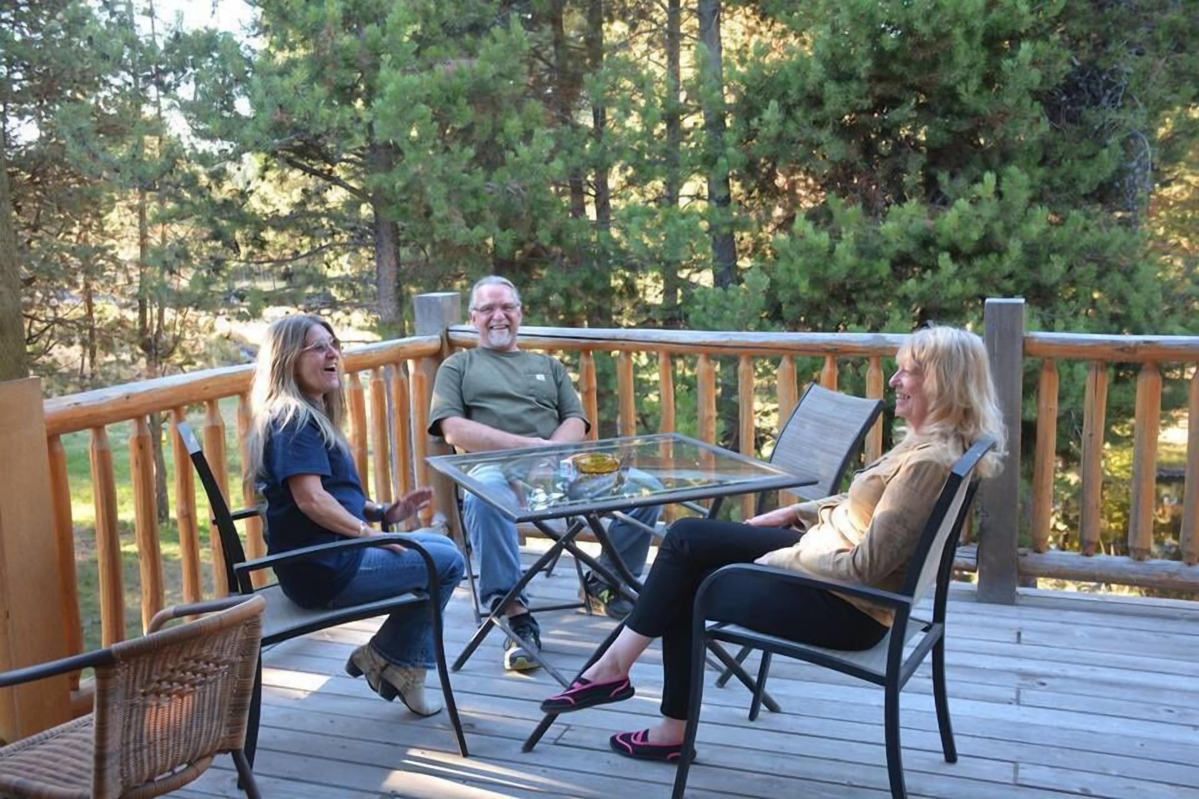 A wooden deck with a glass table and chairs, surrounded by trees.