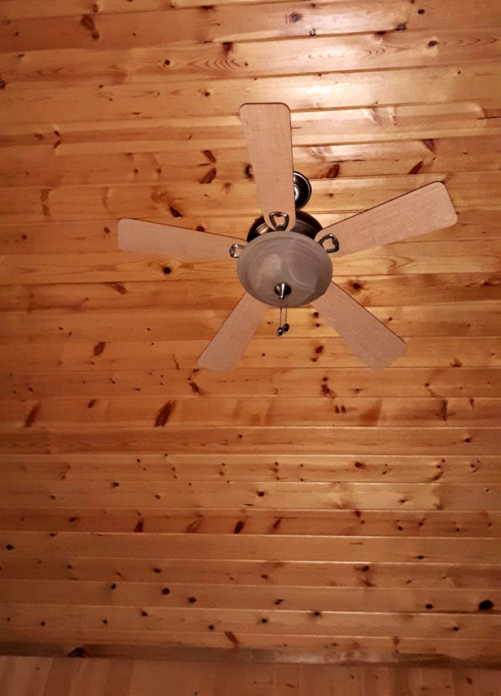 A ceiling fan with a wooden finish in a room with wooden paneling.