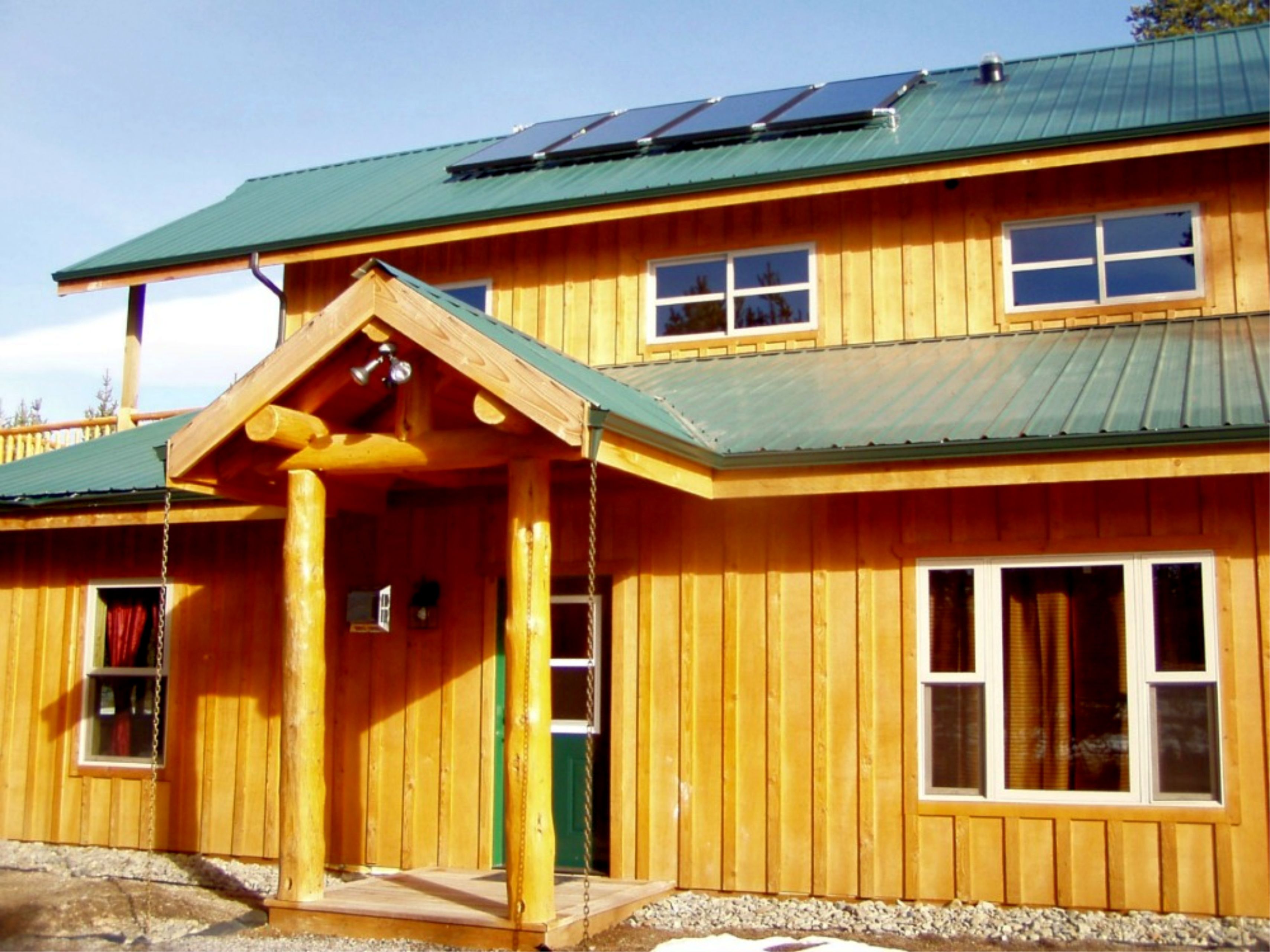 Edificio de madera de dos pisos con techo verde, paneles solares y un porche cubierto con un columpio.