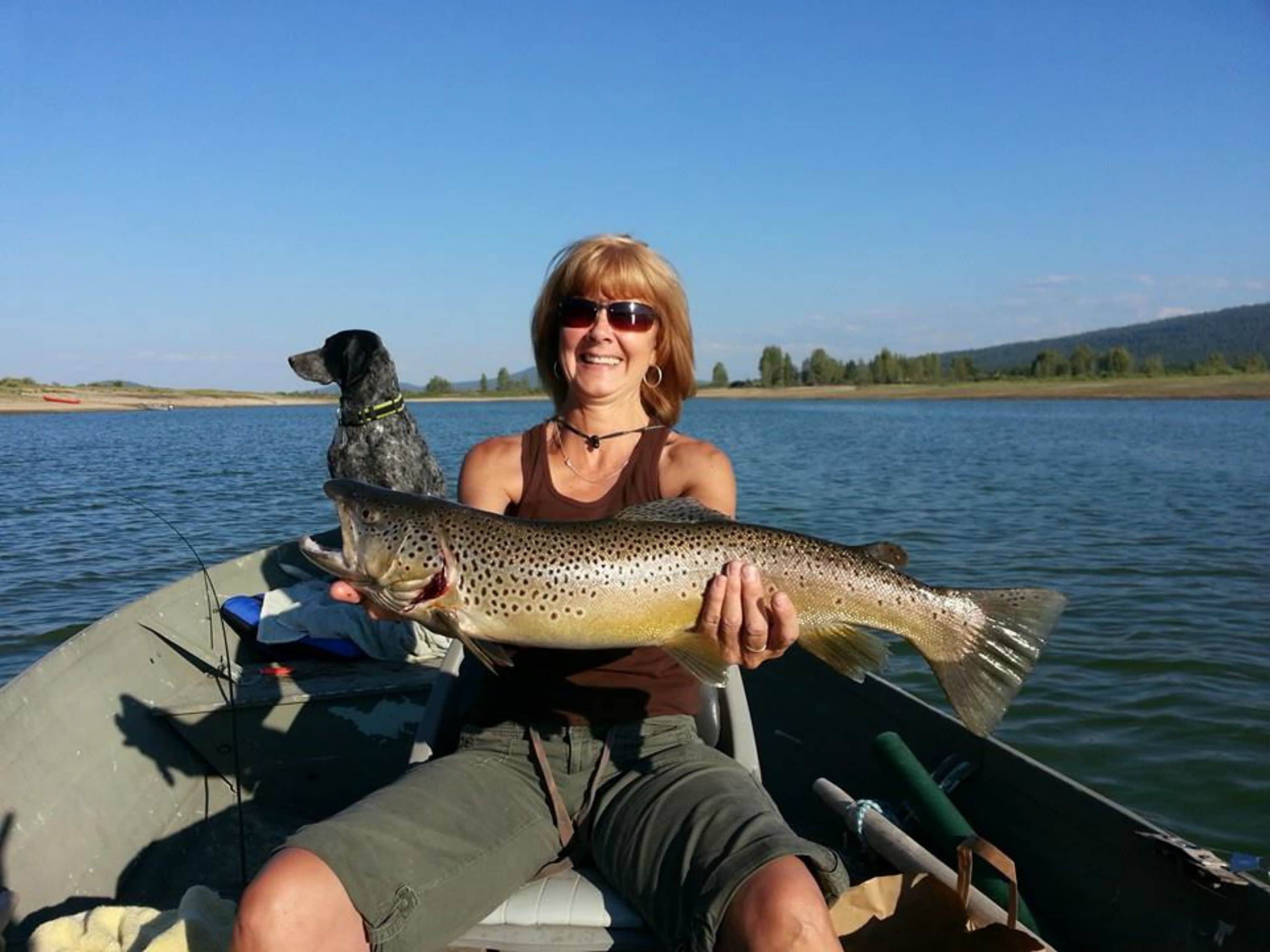 A person holding a fish on a boat with a dog nearby.