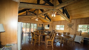 A spacious wooden interior with a large dining table surrounded by chairs, a kitchen area, and a balcony with a wooden railing. - DiamondStone Guest Lodges (La Pine)