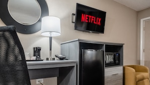 A hotel room with a TV displaying 'NETFLIX', a desk with a lamp, a coffee maker, a phone, and a microwave. - Super 8 by Wyndham Downtown Gatlinburg at Convention Center (Gatlinburg)